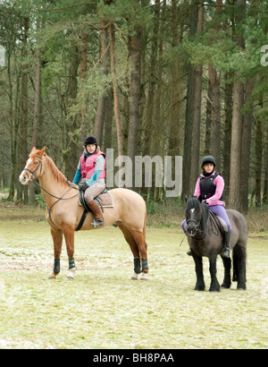 Zwei Mädchen im Teenageralter Reiten ihre Pferde und Pony durch den Wald; Thetford Forest, Norfolk, Großbritannien Stockfoto