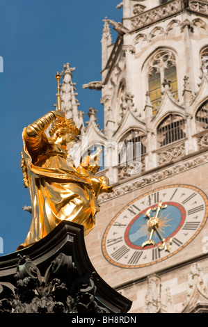 Goldene Statue der Heiligen Maria mit Münchner neuen Rathaus-Uhr als Kulisse. Stockfoto