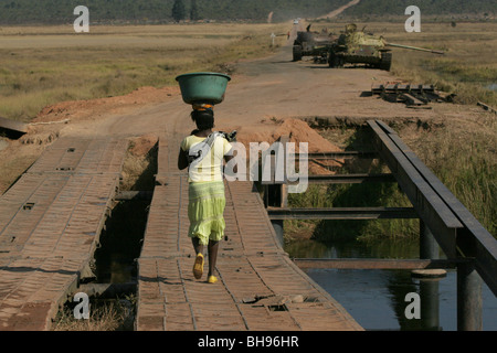 Angolanischen Frau mit Korb auf dem Kopf geht auf zwei Tanks, die Longa, Angola, Afrika aufgegeben wurden. Stockfoto