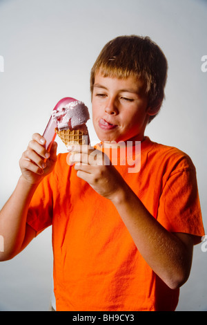 Leckte sich die Lippen in Erwartung, stellt ein fröhlicher zehn Jahre alter Junge eine Kugel Eis in ein Waffelhörnchen. Stockfoto