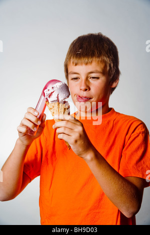 Leckte sich die Lippen in Erwartung, stellt ein fröhlicher zehn Jahre alter Junge eine Kugel Eis in ein Waffelhörnchen. Stockfoto