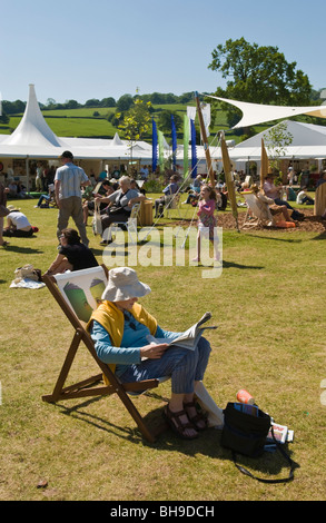 Ältere Frau mit Sonnenhut saß im Liegestuhl lesen Zeitung und entspannen draußen in der Sonne Hay Festival 2009. Stockfoto