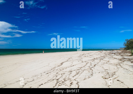 Amity Point Beach Moreton Bay Queensland | NORTH STRADBROKE ISLAND, Queensland, Australien – Ein einsamer Wanderer folgt dem seichten Wasser am Amity Point, während die Gezeitenwunde die sich zurückziehende Hochwasserlinie über den Sand zieht. Mit Blick auf die geschützten Gewässer der Moreton Bay und nicht auf den offenen Pazifik, wurde der Strand nach dem Vermessungsschiff des Entdeckers John Oxley benannt, und seine Küste liegt im Quandamooka Country, das den traditionellen Besitzern als Minjerribah bekannt ist. Stockfoto