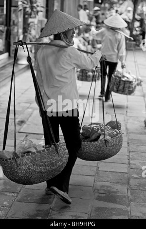 Vietnamesische Frauen mit asiatischen Stil konischen Hüten die Körbe auf den Schultern und ihre Waren verkaufen auf den Straßen von Hanoi im Norden Vietnams. Stockfoto