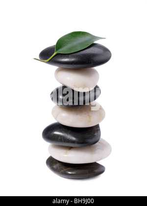 Black And White Stones gestapelt mit grünen Blatt an der Spitze auf weißem Hintergrund Stockfoto