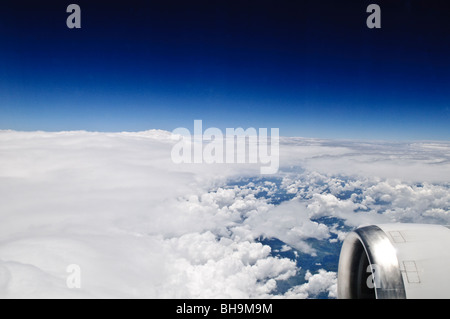 Flugzeugfenster Blick über Wolken Sydney Australien // SYDNEY, Australien — Ein Blick aus einem Flugzeugfenster fängt eine riesige Weite flauschiger weißer Wolken darunter ein, mit einem klaren, tiefblauen Himmel darüber. Das helle Sonnenlicht beleuchtet die Wolkenlandschaft und bietet eine ruhige Luftperspektive, wobei ein Teil des Triebwerks unten rechts sichtbar ist. Stockfoto