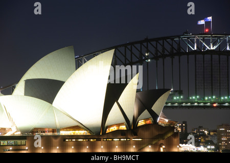 Sydney Opera House und Harbour Bridge bei Nacht Sydney Australien / SYDNEY, Australien – die beleuchteten Dachschalen des Sydney Opera House stehen nachts vor dem Stahlbogen der Sydney Harbour Bridge. Architekt Jørn Utzon löste die technische Herausforderung dieser ineinander greifenden Tresore, indem er ihre Geometrie von der Oberfläche einer einzigen Kugel ableitete und die Lösung zwischen 1957 und 1962 mit Ove Arup & Partners durcharbeitete. Dieser mathematische Durchbruch ermöglichte es, die Betonrippen aus standardisierten Elementen vorzufertigen und vor Qu mit 1.056.006 Chevron-gemusterten Keramikfliesen zu verkleiden Stockfoto