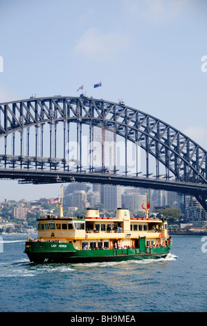 Sydney Harbour Bridge and Ferry Sydney Australien | SYDNEY, Australien – die Fähre von Lady Herron führt unter der Sydney Harbour Bridge am Port Jackson vorbei, eingerahmt von der Skyline von North Sydney. Das 1979 gebaute Schiff gehört zur Lady-Class-Flotte, die von Sydney Ferries betrieben wird. Winzige Figuren, die auf dem oberen Bogen der Brücke zu sehen sind, sind Kletterer auf der 1998 für die Öffentlichkeit eröffneten BridgeClimb Touristenattraktion. Stockfoto