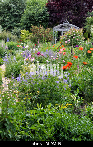 Cranesbills (Geranien), orientalischer Mohn (Papaver Orientale), Rosen (Rosa), Pfingstrosen (Paeonia) und Fingerhut (Digitalis) mit Garten Pavillon. Design: Stockfoto