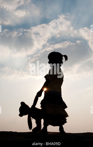 Kleine Inderin und ihr Teddy Bär bei Sonnenuntergang. Silhouette. Indien Stockfoto