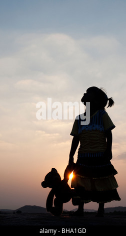 Kleine Inderin und ihr Teddy Bär bei Sonnenuntergang. Silhouette. Indien Stockfoto