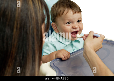 Junge Frau, die Fütterung der jungen im Hochstuhl Stockfoto