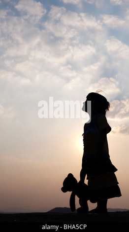 Kleine Inderin und ihr Teddy Bär bei Sonnenuntergang. Silhouette. Indien Stockfoto