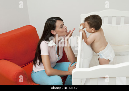 Junge Frau auf Sessel weht Kuss Baby jungen in Krippe Stockfoto