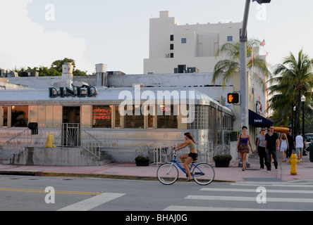 Eine junge Frau fährt ein Strand Fahrrad vorbei an der 11th Street Diner an der Washington Avenue in sonnigen schönen South Beach Miami Beach, FL Stockfoto