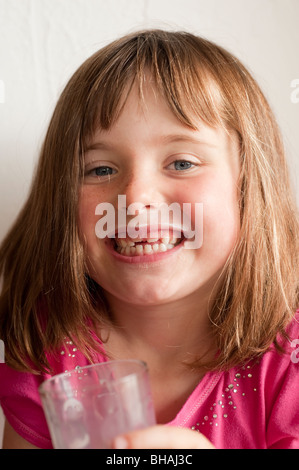 kleines Mädchen, das durch fehlende zwei Vorderzähne genießen Glas Milch lächelt Stockfoto