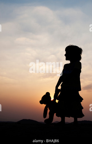 Kleine Inderin und ihr Teddy Bär bei Sonnenuntergang. Silhouette. Indien Stockfoto