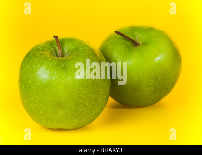 Obst auf einem gelben Hintergrund mit einem Farbverlauf fotografiert. Zwei grüne Äpfel auf einem gelben Hintergrund. Stockfoto