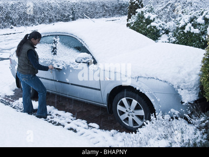 Eine junge Frau versucht, öffnen Sie Schnee bedeckt geparkten Autotür in schweren winterlichen Zustand des Schneefalls auf Bäumen, Straßen und Fahrzeug. Stockfoto