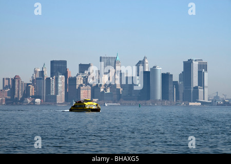 Ein Wassertaxi Geschwindigkeiten über das Wasser an einem dunstigen sonnigen Tag mit der unteren Manhattan Skyline im Hintergrund Stockfoto