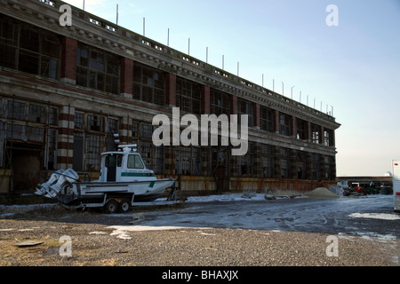 Ein Boot auf einem Anhänger parkte vor einem verfallenen Gebäude auf Ellis Island, New York Stockfoto