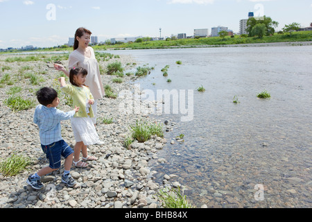 Japan, Tokyo Präfektur, Mutter und Kinder werfen Kieselsteine in Fluss Stockfoto