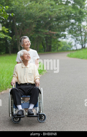 Japan, Tokyo Präfektur, älteres Paar im Park, Mann sitzt im Rollstuhl, nachschlagen, Lächeln Stockfoto