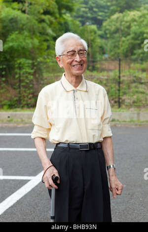 Japan, Tokyo Präfektur, Senior Mann mit Spazierstock, stehend auf Straße, lächelnd, Nahaufnahme Stockfoto