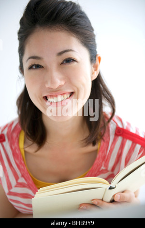 Japan, Osaka Präfektur, junge Frau Holding Buch, Lächeln, Porträt, Nahaufnahme Stockfoto