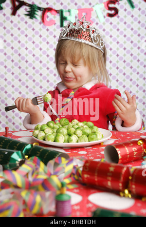 Eine drei Jahre alte sitzen an einem Tisch mit Weihnachtsschmuck und einem Teller voller Sprossen ziehen ein Gesicht in Ekel. Stockfoto