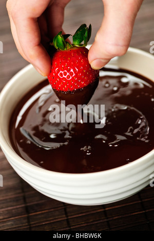 Hand, die frischen Erdbeere in geschmolzene Schokolade eintauchen Stockfoto