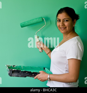 Hübsche Frau mit Farbwanne und Walze abgeschlossen Malerei hellen smaragdgrünen Farbe auf Wand und zufrieden mit der Arbeit. Stockfoto
