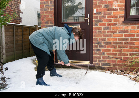 Frau löscht Schnee vom Laufwerk ihres Hauses Stockfoto