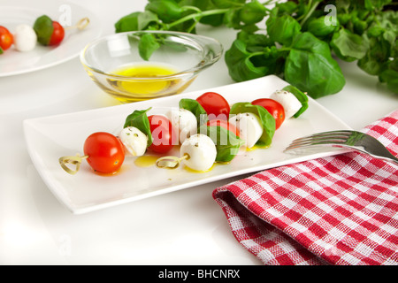 Salat Caprese sticks - spitted Cherry-Tomaten, Mozzarellakugeln und Basilikum-Blätter auf einer rechteckigen Platte, verfeinert mit Olivenöl Stockfoto