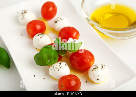 Mozzarella Käsekugeln aufgespießt mit Tomaten und Basilikum mit Olivenöl und Kräutern auf einer Platte Stockfoto