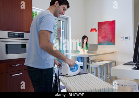 Bügeln, während Frau Laptop benutzt Mann Stockfoto