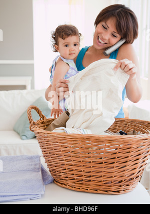 Hispanische Mutter Holding Tochter, am Telefon und Wäsche Stockfoto