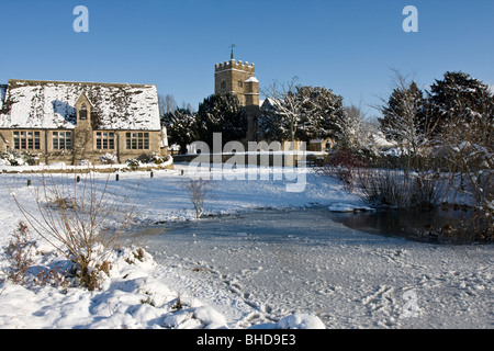 Ducklington Teich, Kirche und alte Schule im Schnee Stockfoto