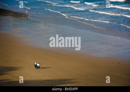 Rückansicht eines nicht identifizierbaren reifen Paares, das auf Klappstühlen an einem verlassenen britischen Strand sitzt und auf das Meer blickt. Stockfoto