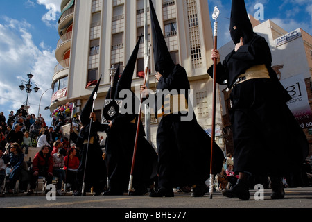 Die Karwoche Teilnehmer trugen eine Tunika und eine Kapuze mit der konische Hut (Capirote) gehen Sie die Straße von Malaga, Spanien. Stockfoto