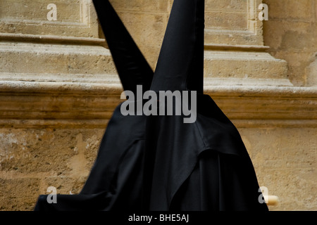 Die Teilnehmer der Karwoche tragen eine schwarze Tunika und eine Kapuze mit Hut, die an Ostern in Málaga, Spanien, an der Kathedrale vorbeigehen. Stockfoto