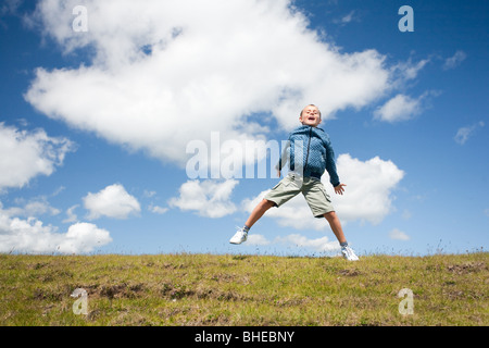 Süßes Kind springen vor Freude in die Luft in einer wunderschönen Landschaft mit blauem Himmel und flauschige Wolken Stockfoto