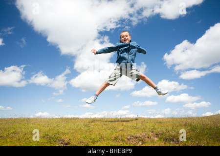 Süßes Kind springen vor Freude in die Luft in einer wunderschönen Landschaft mit blauem Himmel und flauschige Wolken Stockfoto