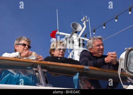 Passagiere auf einer Kreuzfahrt Schiff Uhr Aktivitäten als Schiff zu segeln bereitet. Mast und Schiffshorn im Hintergrund. Stockfoto