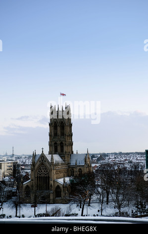 Doncaster Minster erhebt sich im Winter über der Stadt, sein historischer gotischer Turm überblickt schneebedeckte Dächer unter klarem blauem Himmel. Stockfoto