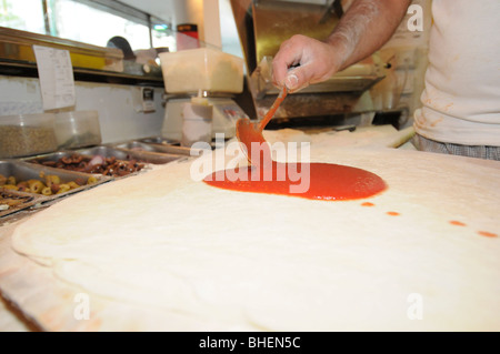 Stadien der Pizza Vorbereitung Spreading Tomatensauce auf die rohen Pizzateig Stockfoto