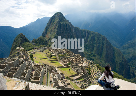 Eine Frau sitzt auf einem Felsvorsprung, bewundern Sie die Aussicht über Machu Picchu und der näheren Umgebung, Peru Stockfoto