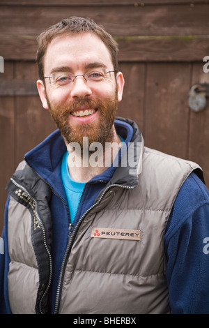 Ein bärtiger Mann lächelt vor einer Holzhütte. Stockfoto