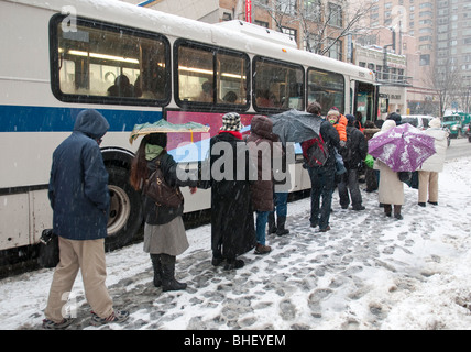 Menschen warten auf einen Bus während eines Schneesturms in New York City an Bord Stockfoto