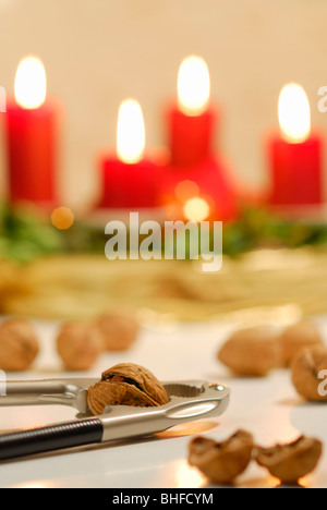 Nussknacker und Walnüsse mit Adventskranz mit vier brennenden Kerzen im Hintergrund Stockfoto